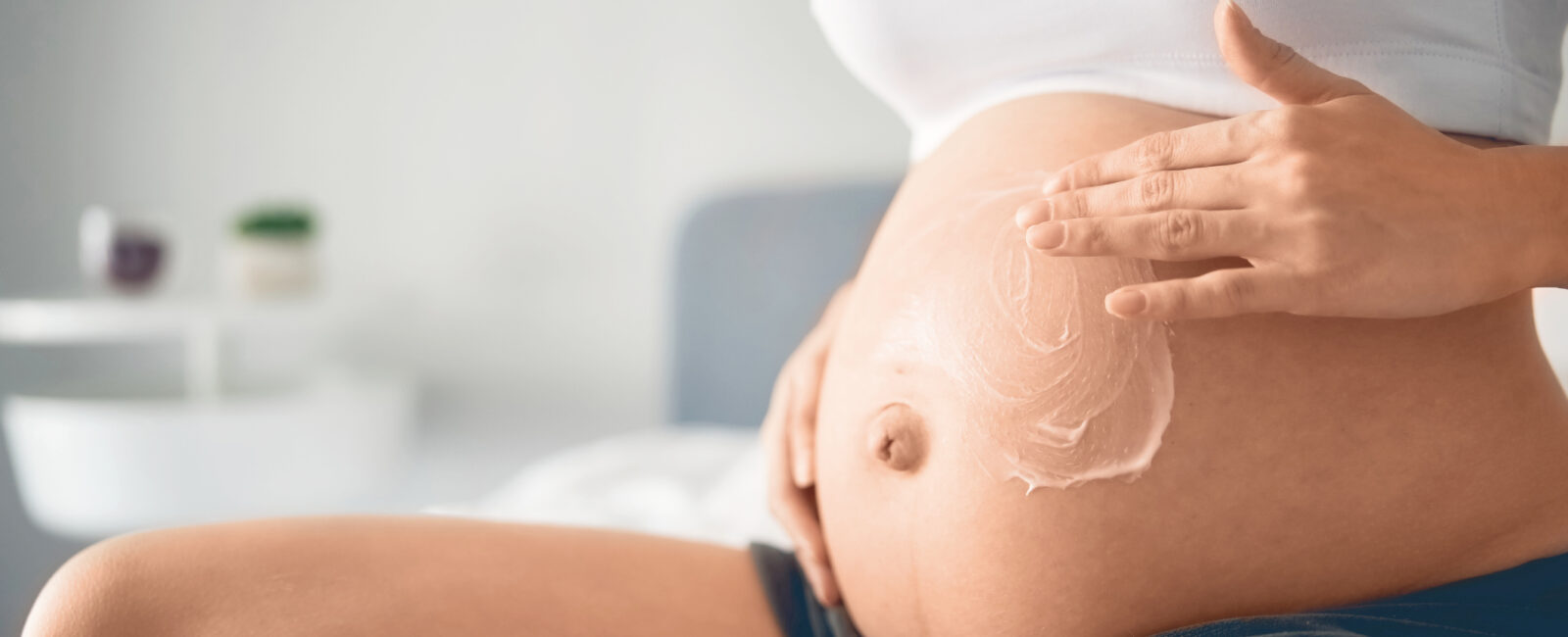 Auf dem Bild ist eine Schwangere Frau zu sehen die mit Hautpflege Schwangerschaftsstreifen vorbeugen möchte.