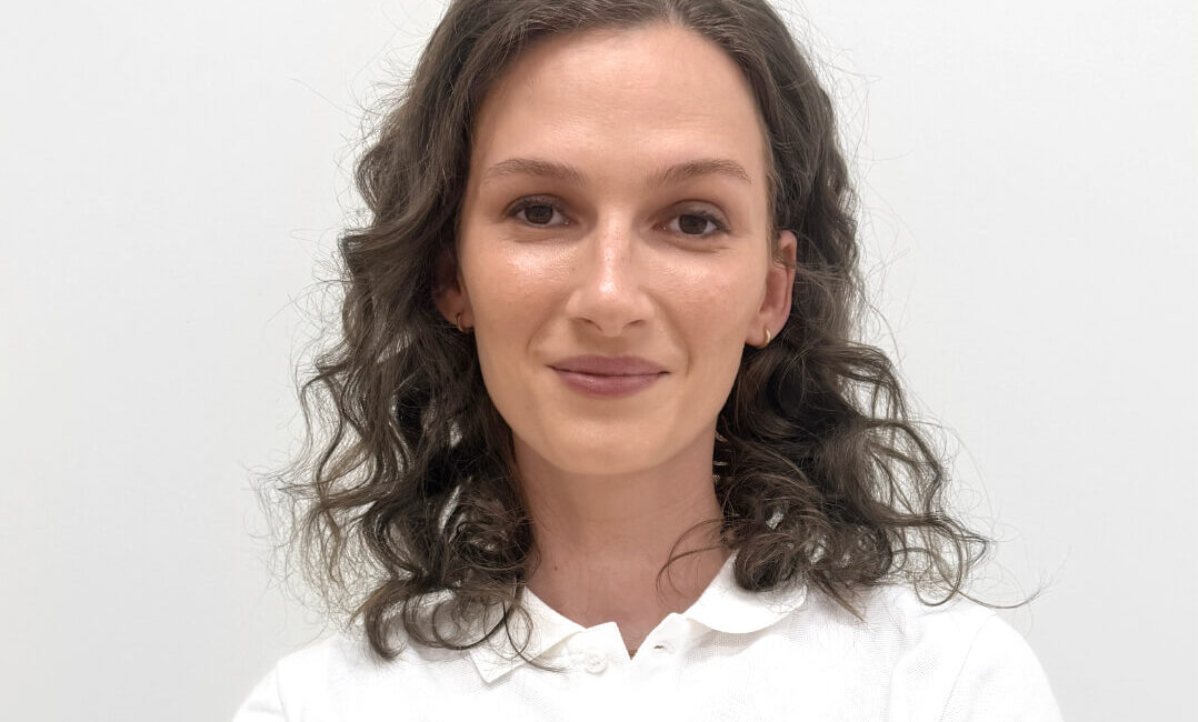 Dr. Alica Pistekova ist Ärztin im Dermacare Insitut Wien. Sie hat braune, lockige Haare und lächelt im weißen Hemd in die Kamera.