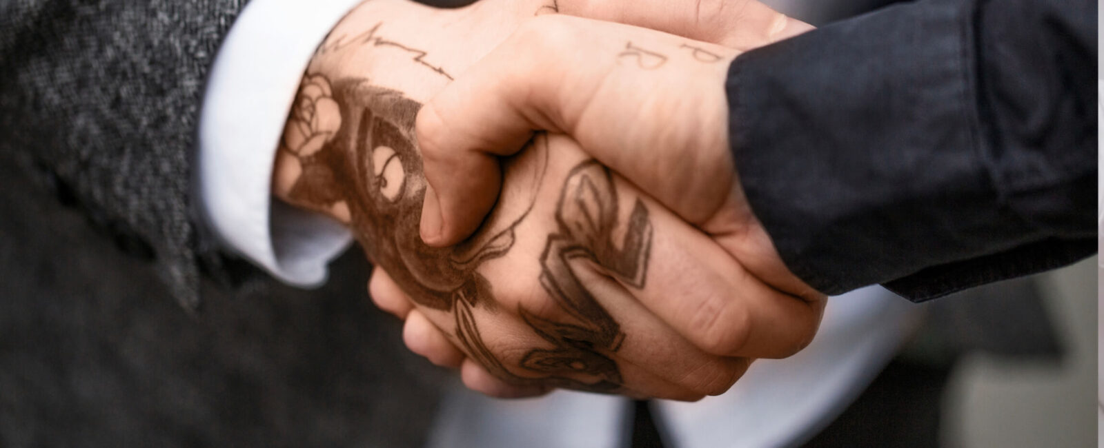 Auf dem Bild sieht man wie Tattoos im Job auch hin und wieder akzeptiert werden können. Zwei personen mit Tattoos auf der Hand schütteln sich die Hand.