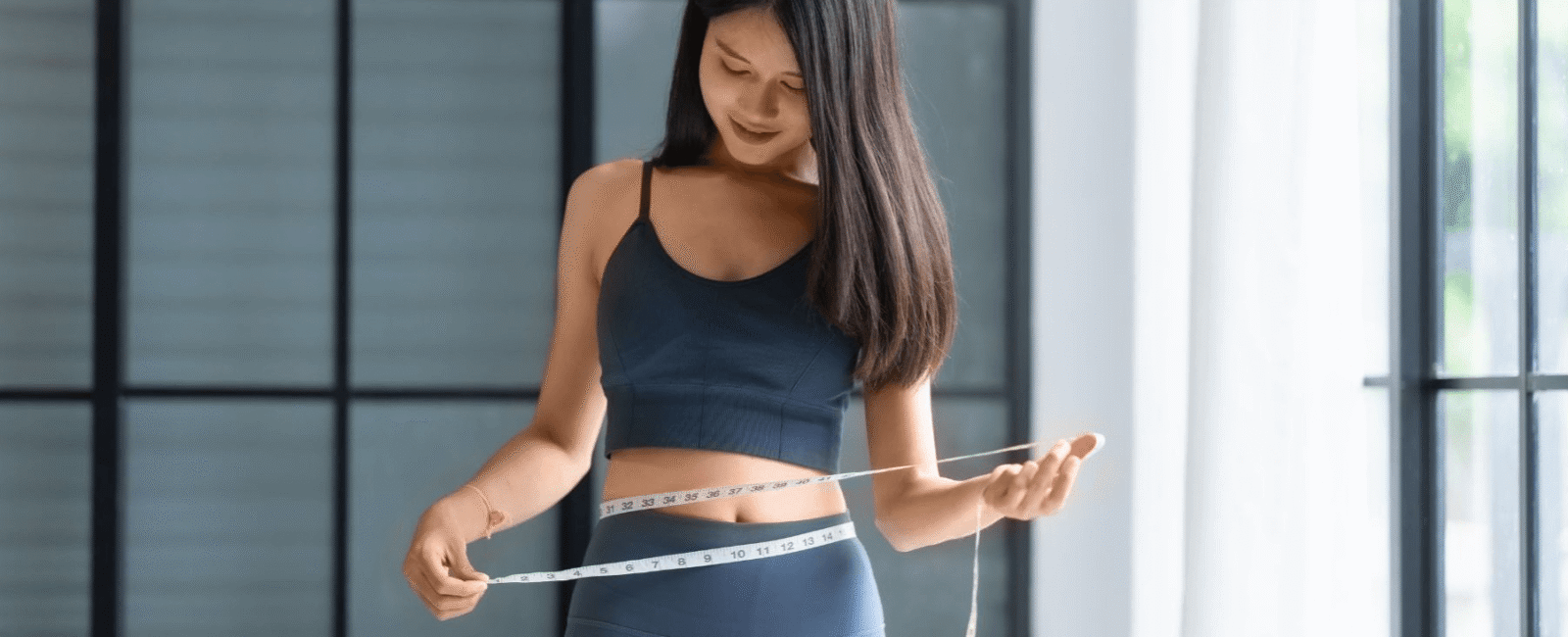 Im Bild geht es um das Abnehmen nach Weihnachten. Man sieht eine Frau die mit einer Maßband ihren Bauchumfang abmisst. Sie sieht sehr schlank aus.