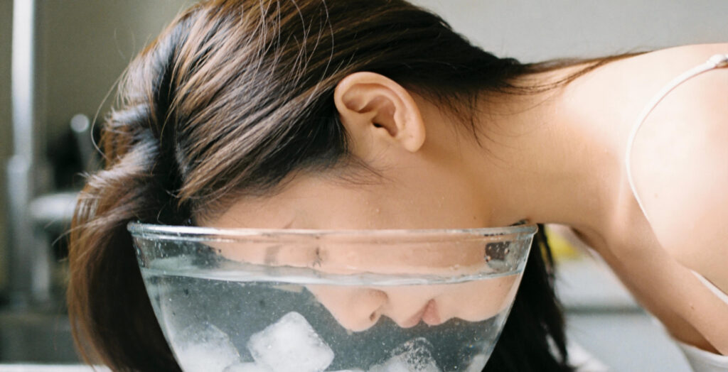 Eine Frau haltet ihr Gesicht in kühles Wasser mit Eiswürfeln. Das ist eine gute Möglichkeit um gegen juckende Haut vorzugehen.